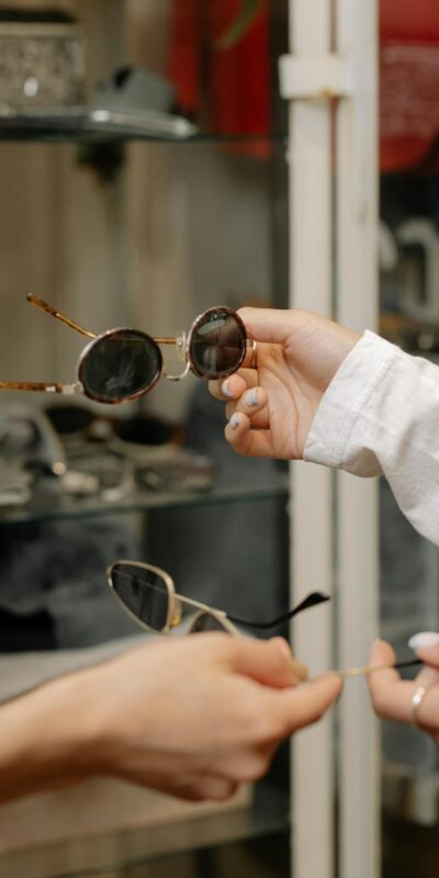 Close-up of hands holding sunglasses, exploring designs in a stylish fashion store.