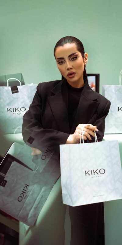 Elegant model posing with branded shopping bags in a modern, stylish setting.