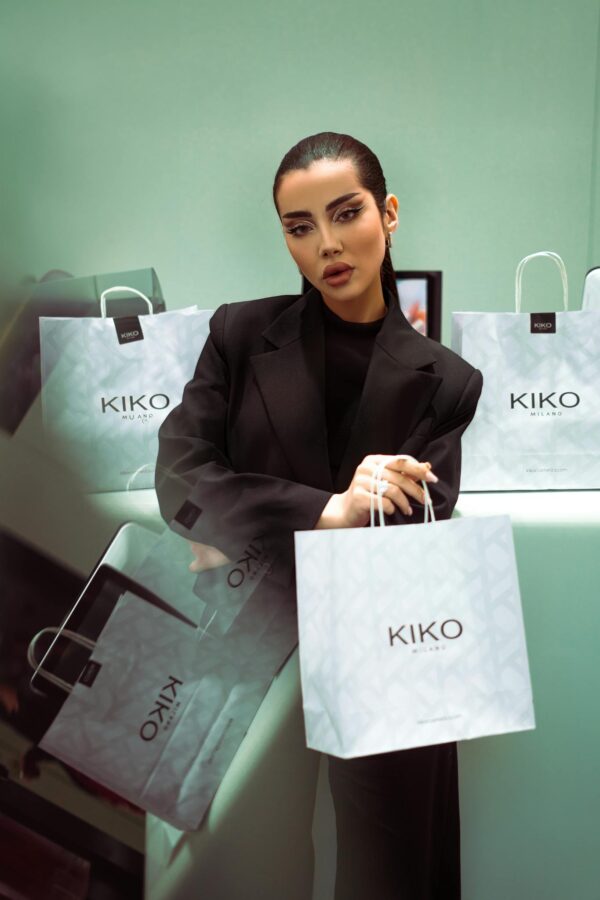 Elegant model posing with branded shopping bags in a modern, stylish setting.